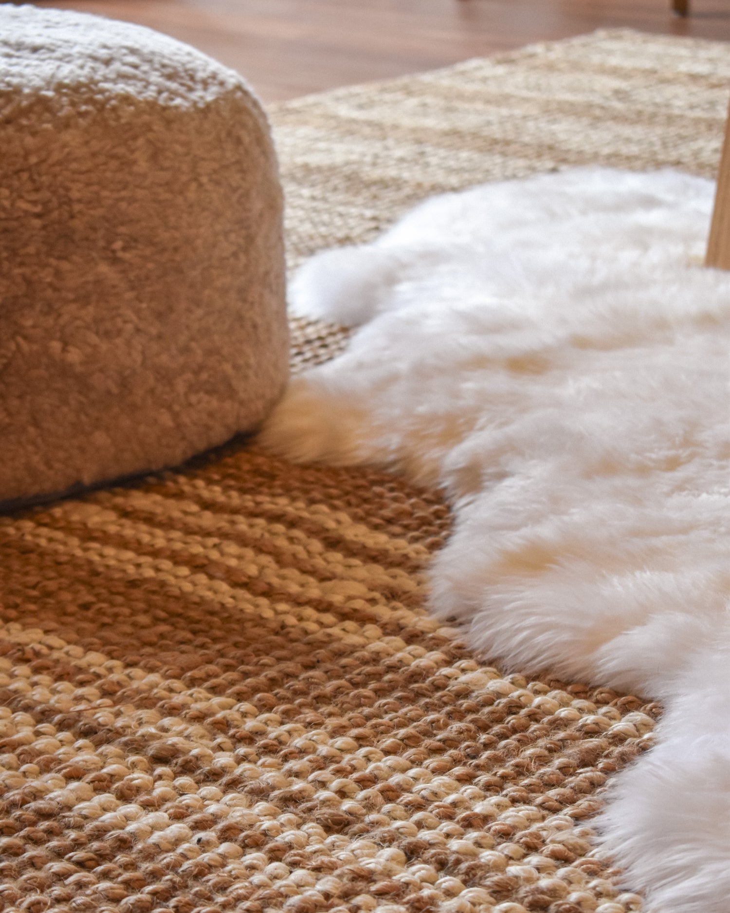 Textured brown rug with a white fur throw on a wooden floor