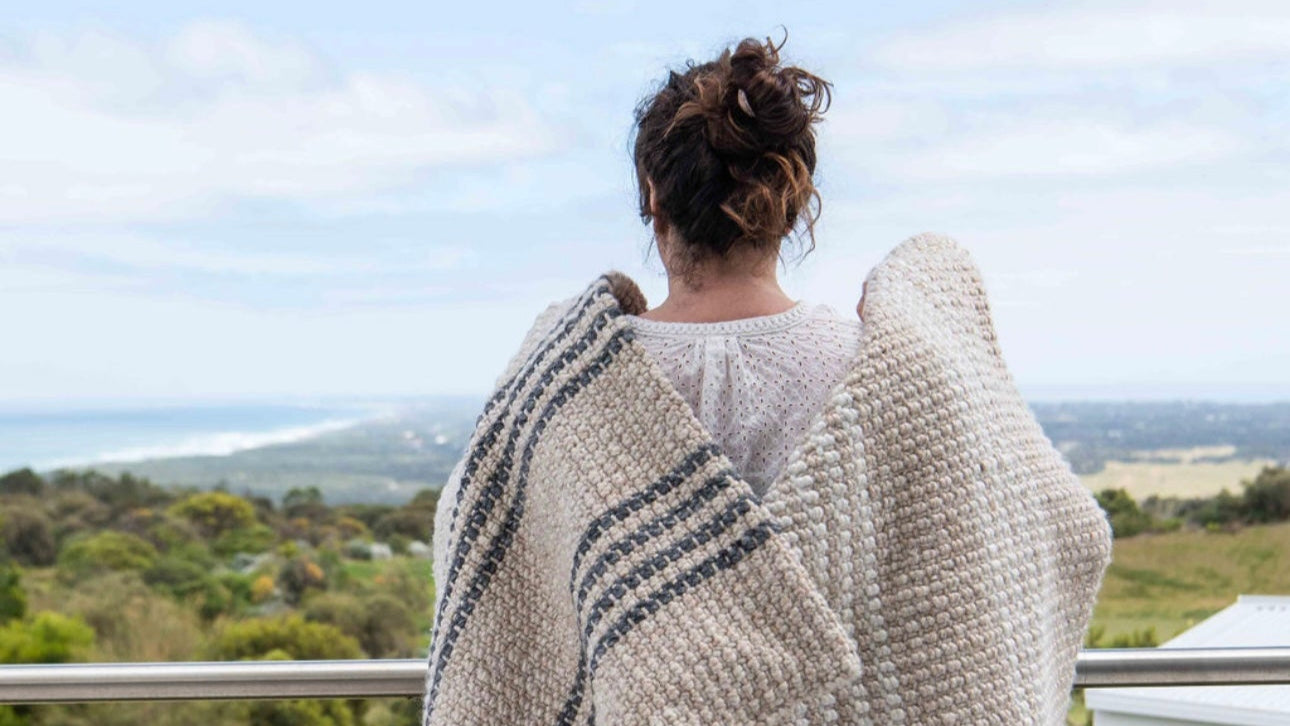 Person wearing a large knitted cardigan overlooking a scenic landscape.