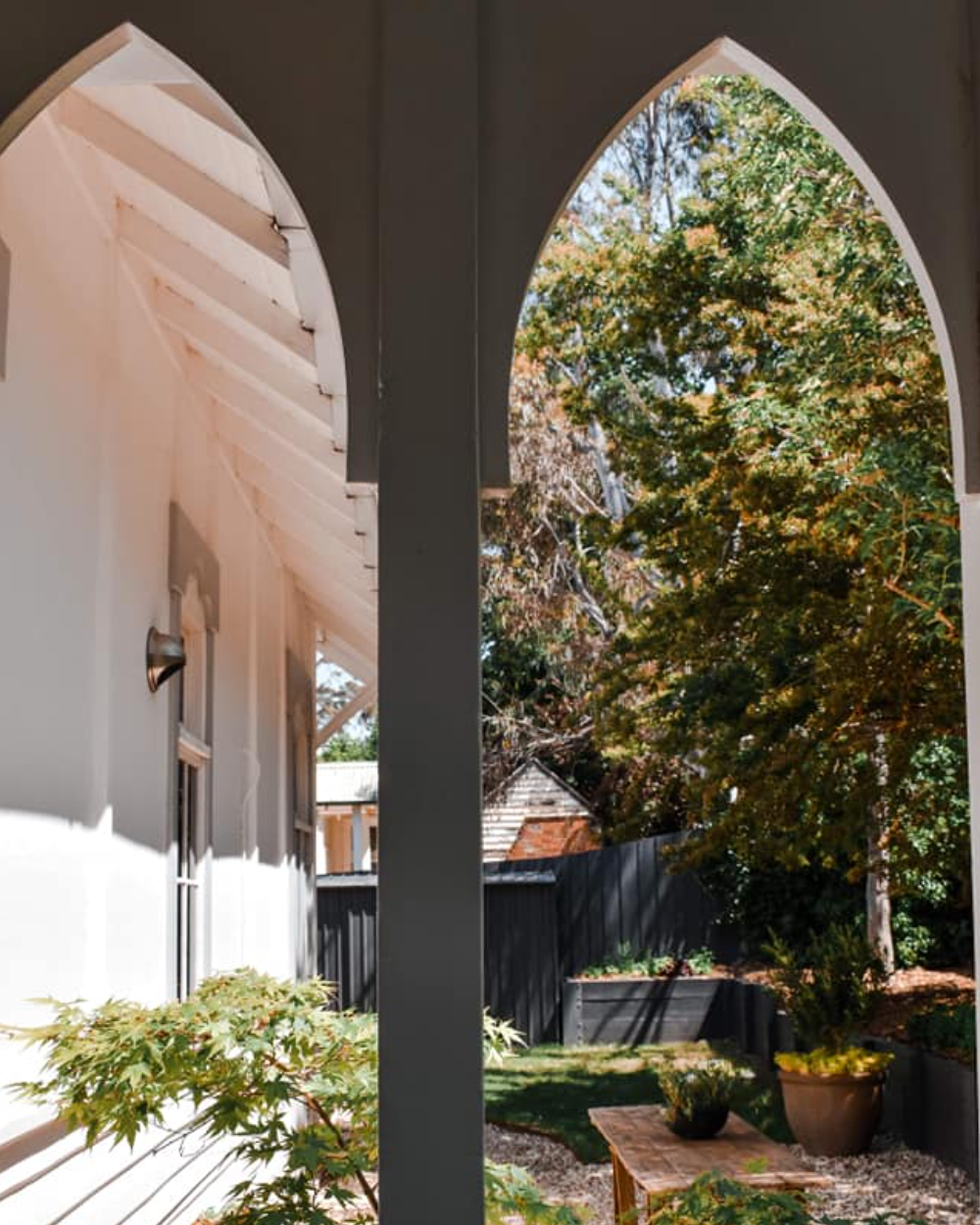View through an archway of a garden with trees and a table.